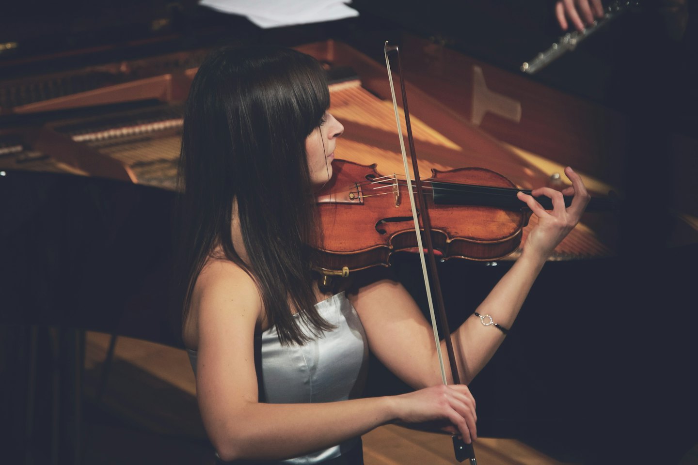 Donna che suona il violino con pianoforte e flauto sullo sfondo.